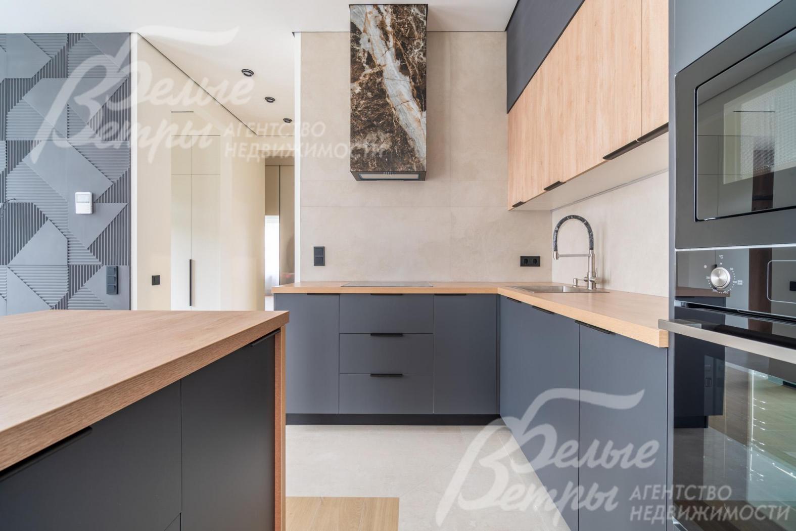 На кухне установлен гарнитур с островом серого цвета, дополненный элементами из древесного ДСП