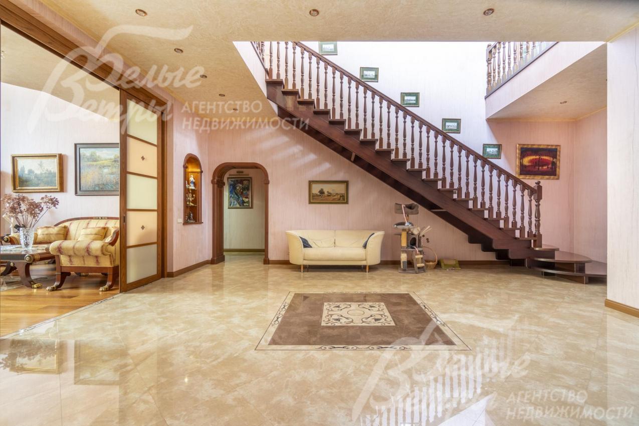 Просторный холл на первом этаже. На второй этаж ведёт деревянная дубовая лестница