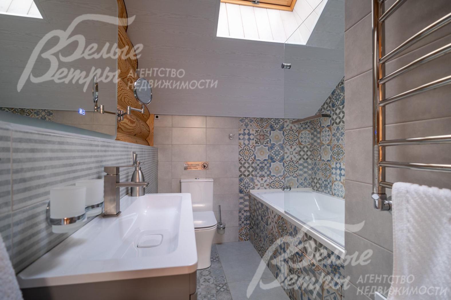 Общий санузел на втором этаже - с ванной, оформлен гладкой плиткой светлого оттенка, зона вокруг ванны выделена декоративной плиткой с орнаментом