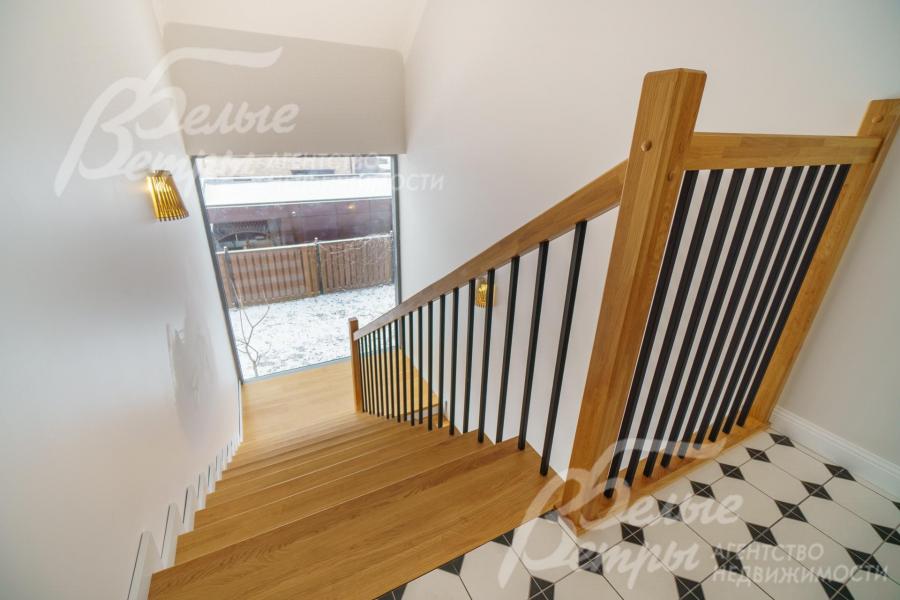 Спуск на первый этаж по лестнице на металлическом каркасе с дубовыми перилами и ступенями, обшитыми дубом. 