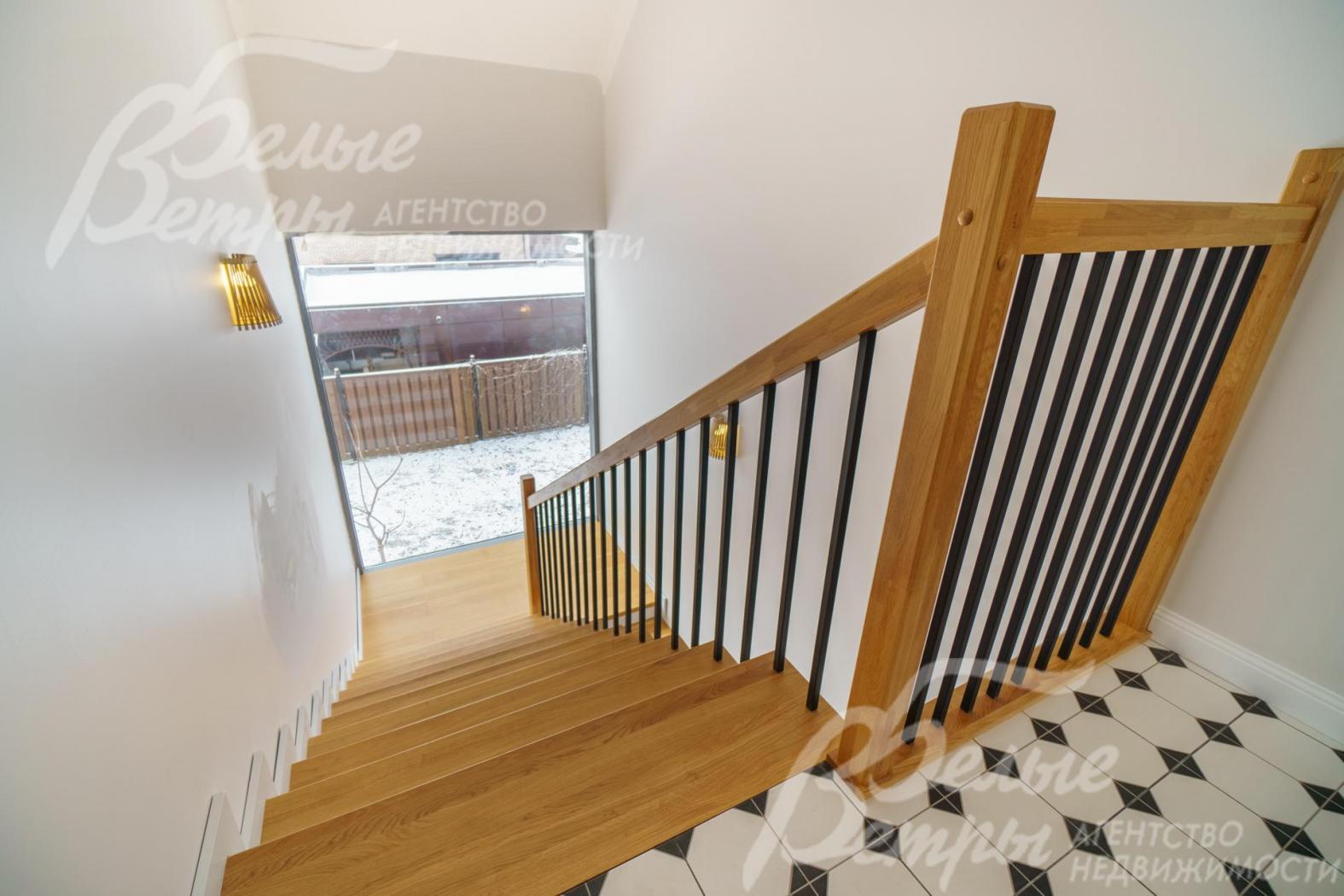 Спуск на первый этаж по лестнице на металлическом каркасе с дубовыми перилами и ступенями, обшитыми дубом. 