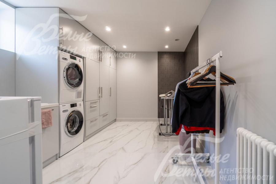 Постирочная на цокольном этаже оборудована стиральной и сушильной машинами, шкафами и гладильной доской