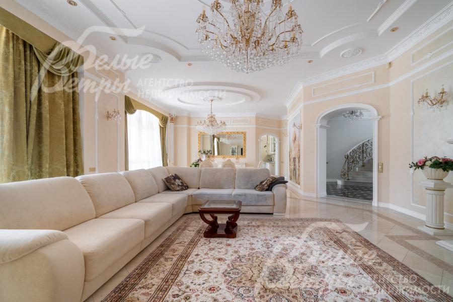Интерьер гостиной дополняют настенные бра, хрустальная люстра, плотные портьеры благородного оливково‑золотистого оттенка
