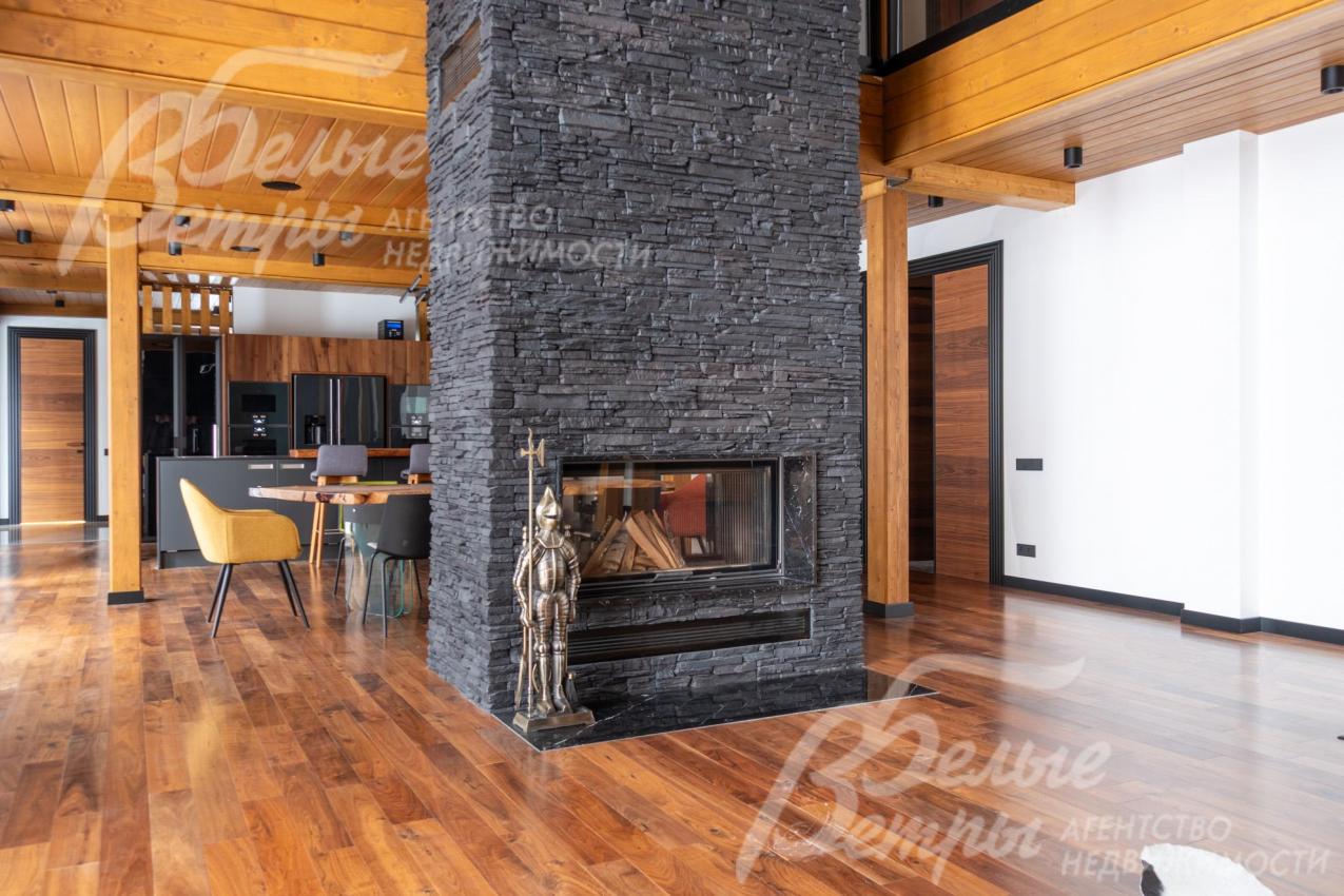 Гостиную украшает двухсторонний камин, облицованный тёмным камнем, который создаёт контраст с тёплыми деревянными элементами интерьера