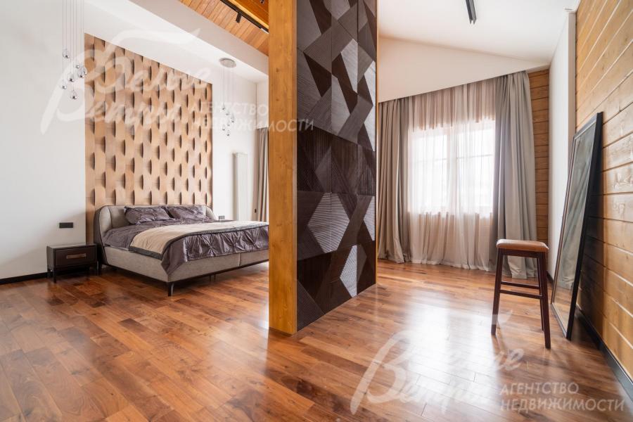 В мастер-спальне кровать расположена у стены с акцентной отделкой — объёмной панелью с геометрическим рельефом в тёплых древесных тонах 