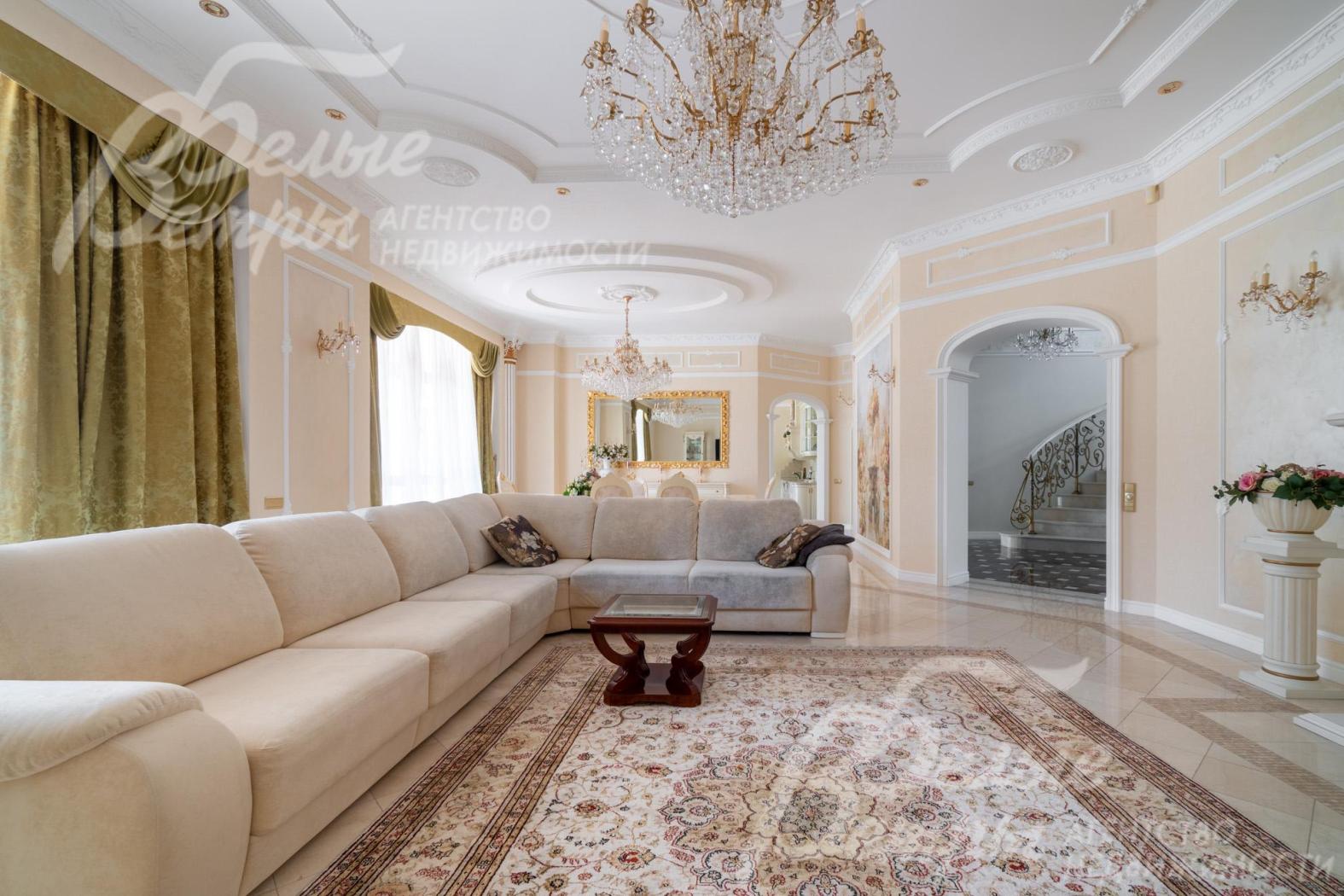 Интерьер гостиной дополняют настенные бра, хрустальная люстра, плотные портьеры благородного оливково‑золотистого оттенка