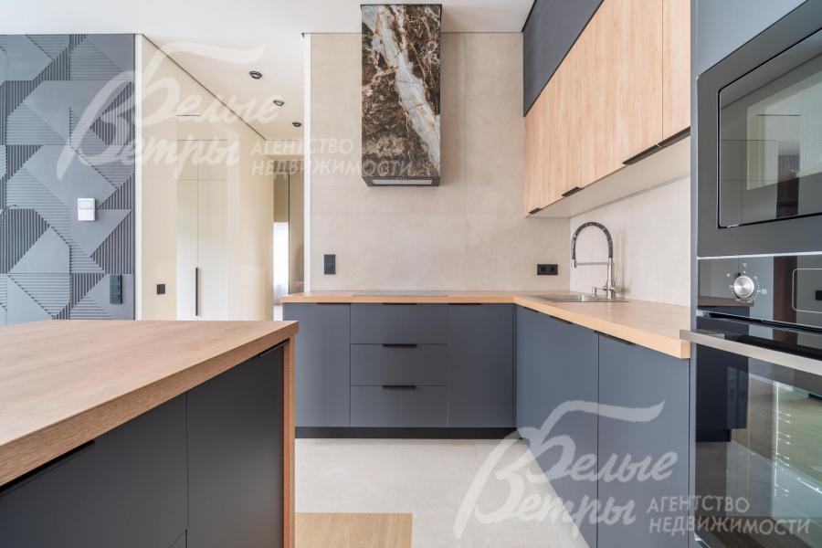 На кухне установлен гарнитур с островом серого цвета, дополненный элементами из древесного ДСП