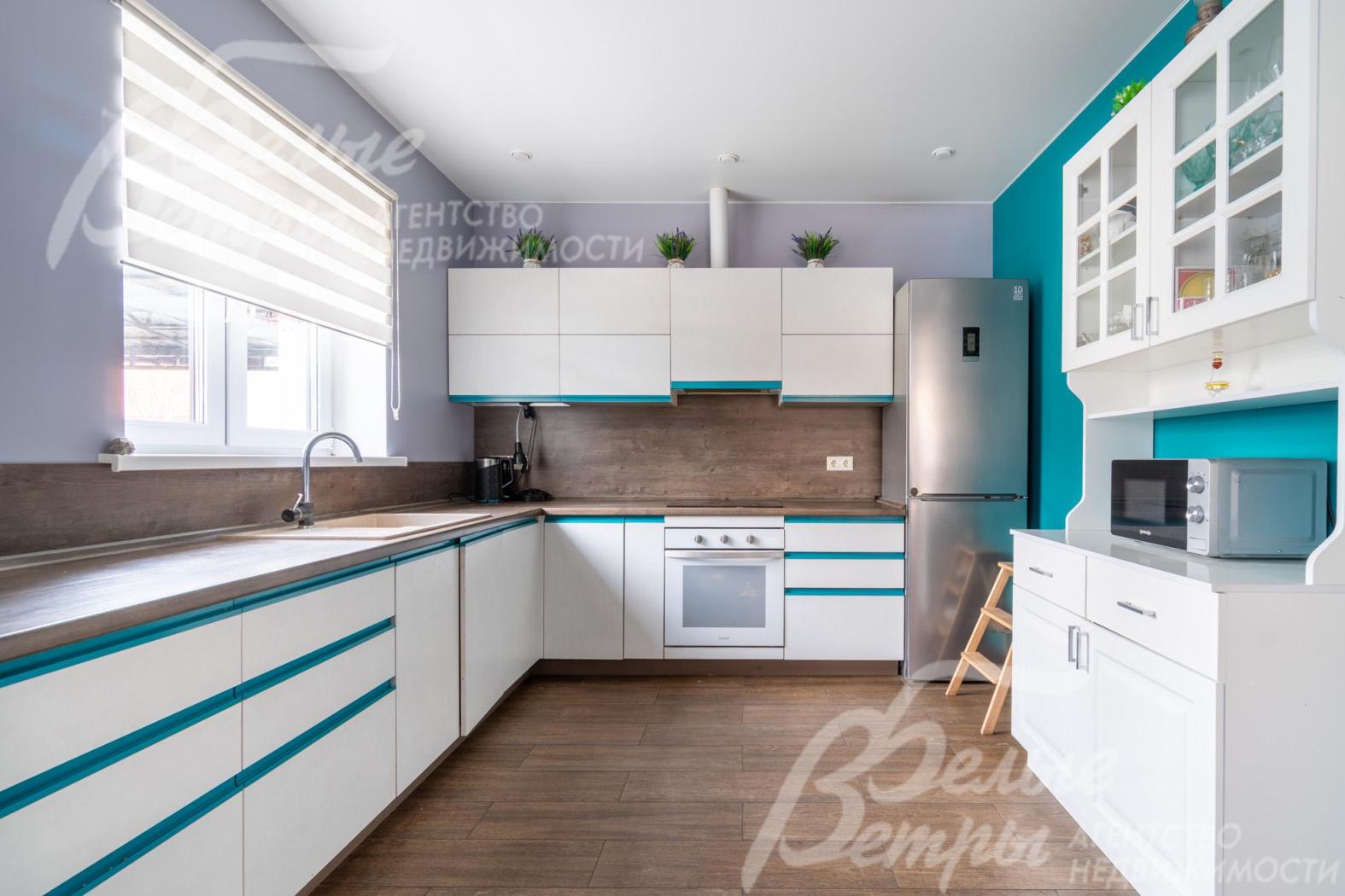 На кухне установлен гарнитур белого цвета с акцентным бирюзовым декором производства «Кухонный дом» со всей встроенной техникой