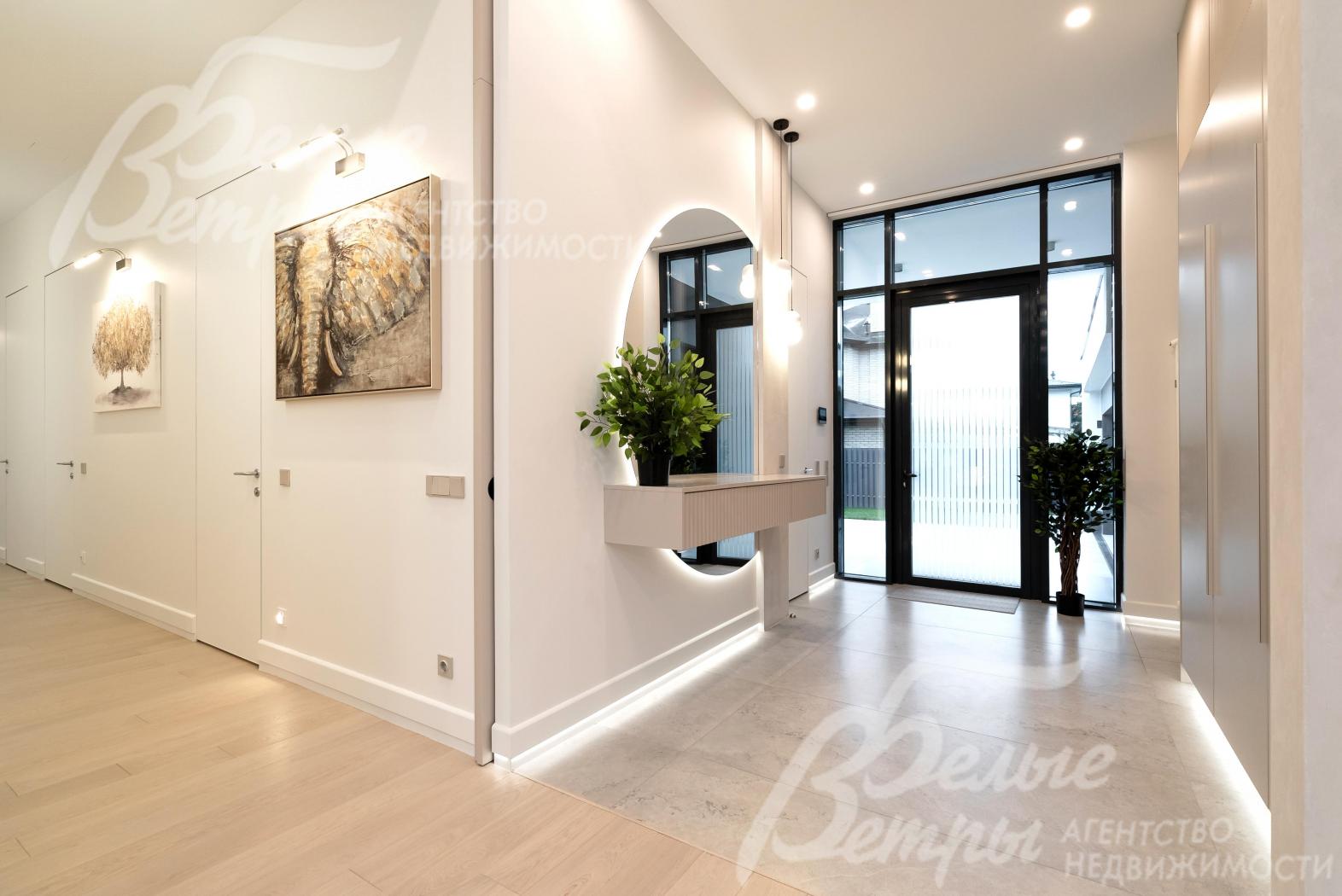 В холле - большая входная дверь со стеклянными элементами, эффектное круглое зеркало с элегантной подсветкой